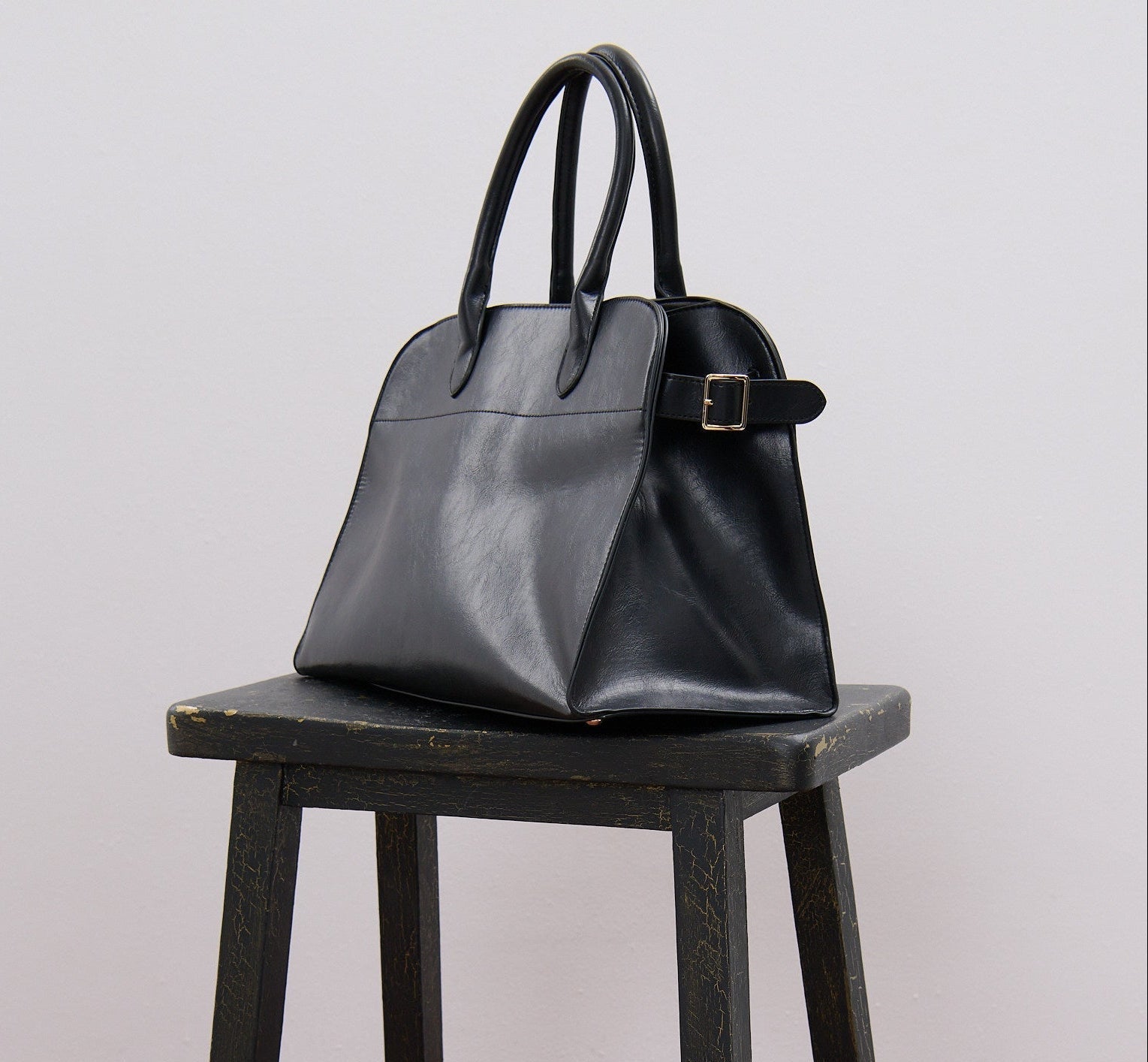 Cool women's black shoulder handbag on a wooden stool against a plain background